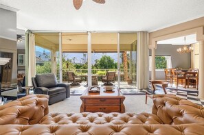 A spacious living area with a large window, a leather sofa, a wooden coffee table, and a dining area with a table and chairs.