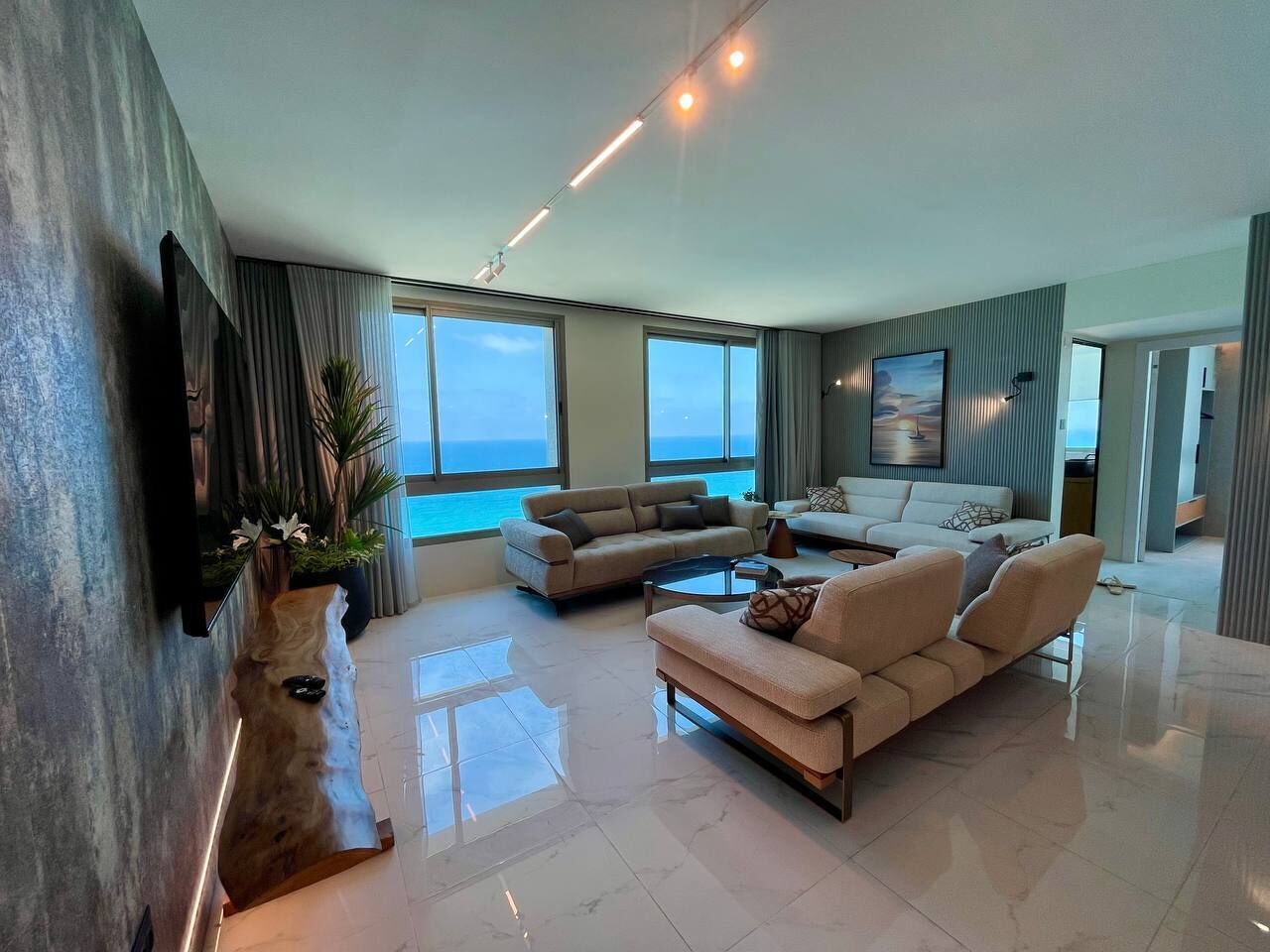 A modern living room with a large window, a flat-screen TV mounted on the wall, and a wooden coffee table.
