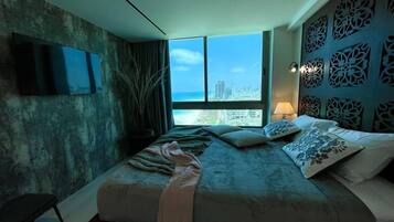 Ein modernes Schlafzimmer mit einem großen Bett, einem an der Wand befestigten Fernseher und Blick auf die Stadt durch große Fenster.