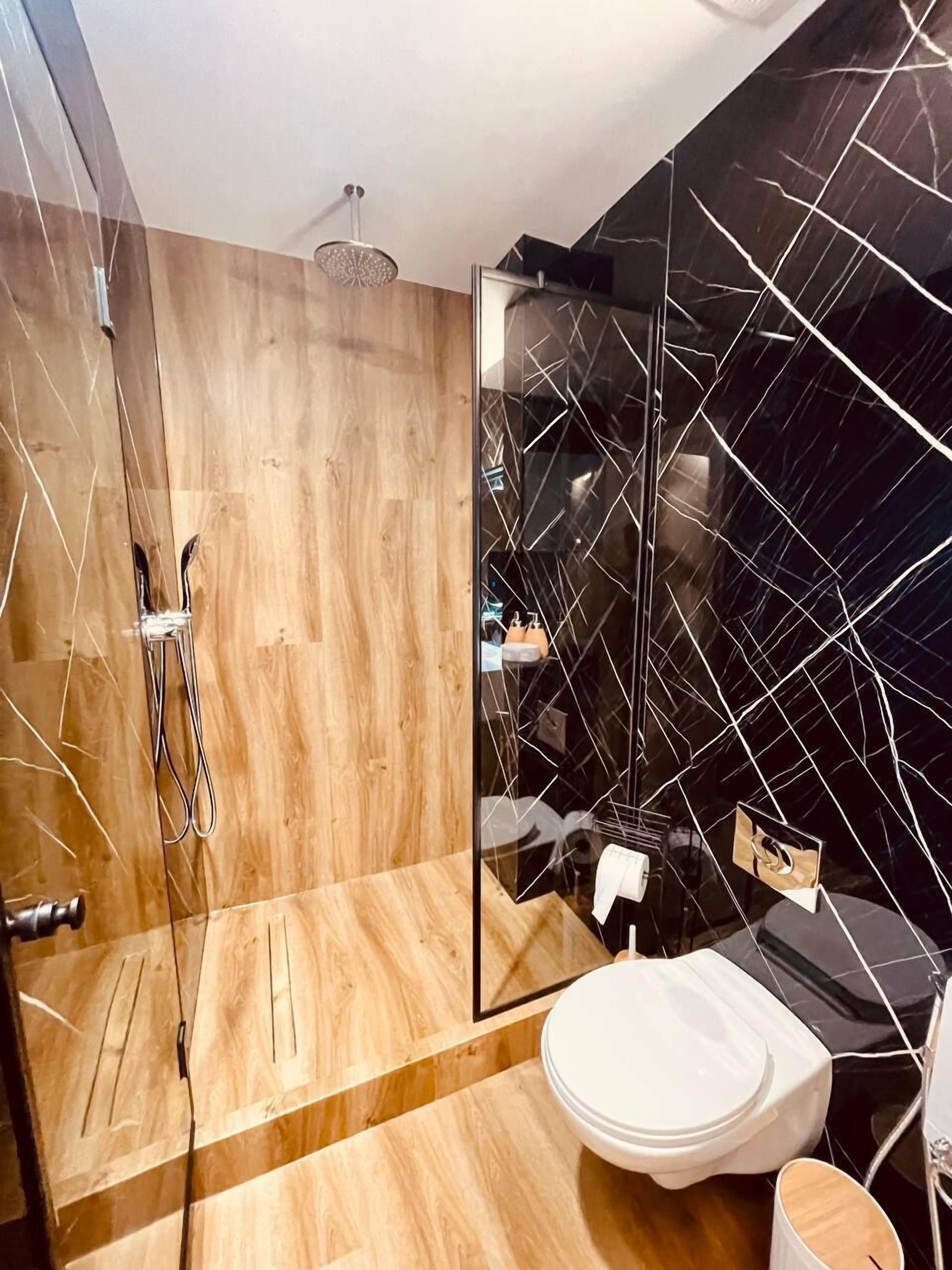 A modern bathroom with a glass shower enclosure, a wooden vanity, and a black tiled wall.