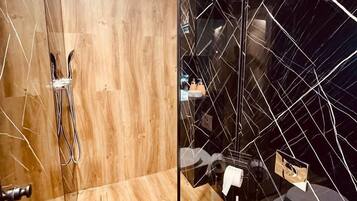 A modern bathroom with a glass shower enclosure, a wooden vanity, and a black tiled wall.