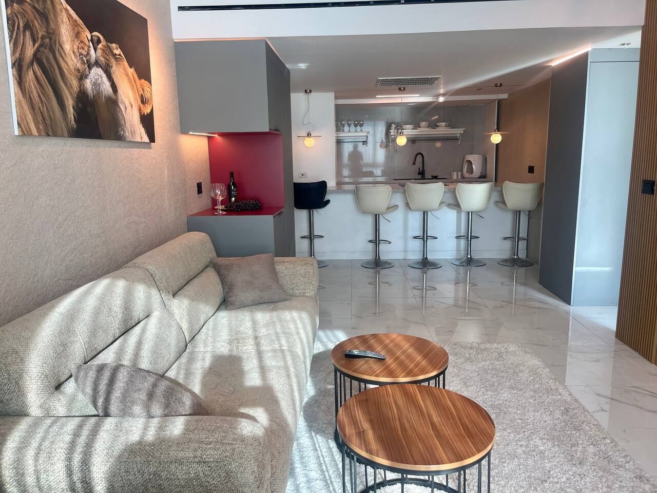 A modern living room with a sofa, two round wooden tables, and a kitchen area with bar stools.