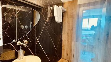 Ein modernes Badezimmer mit Waschtisch aus schwarzem Marmor, einer Duschkabine aus Holz und einer Glastür, die auf einen Balkon führt.