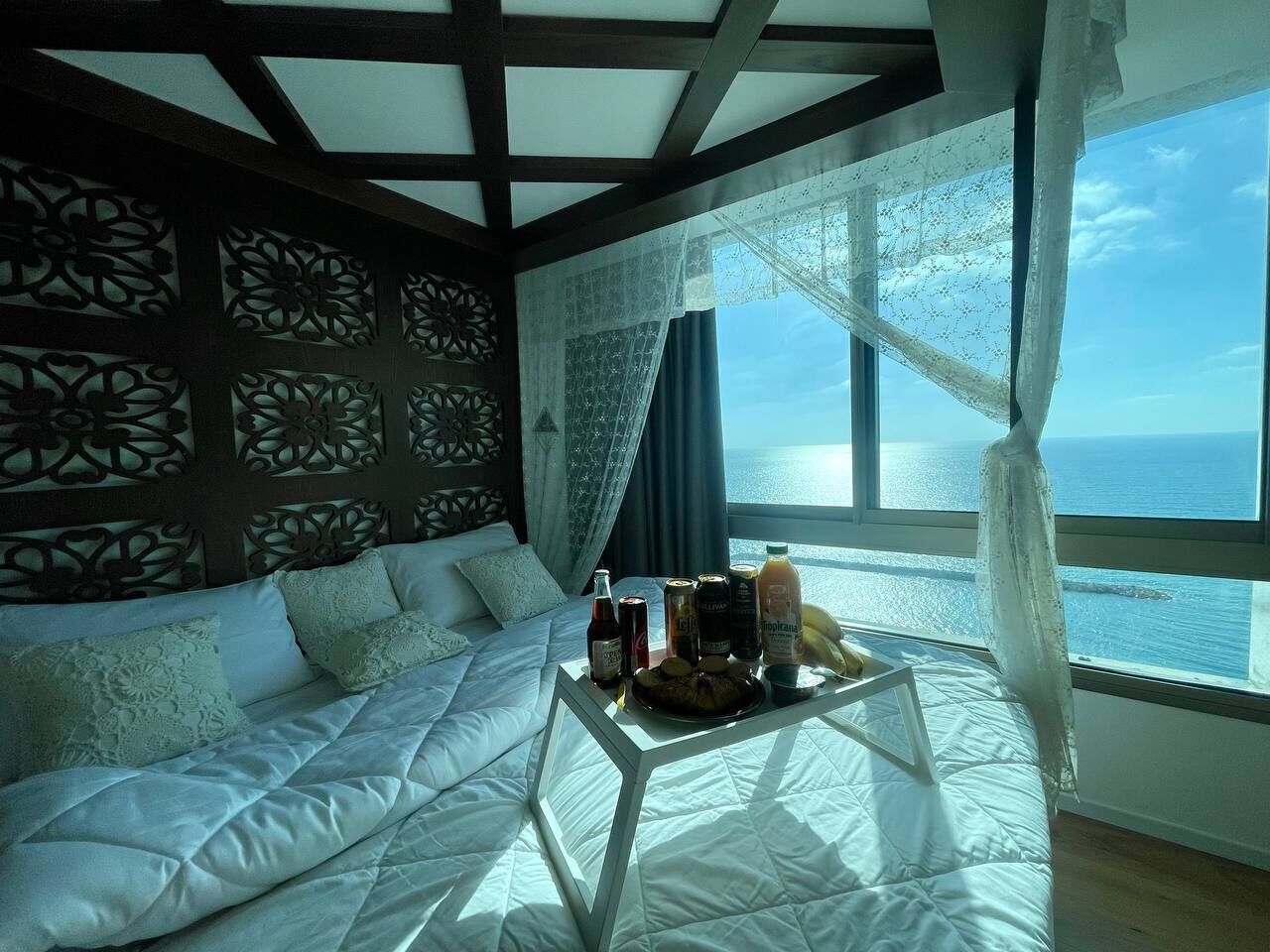 A room with a bed, a table with drinks, and a view of the sea.