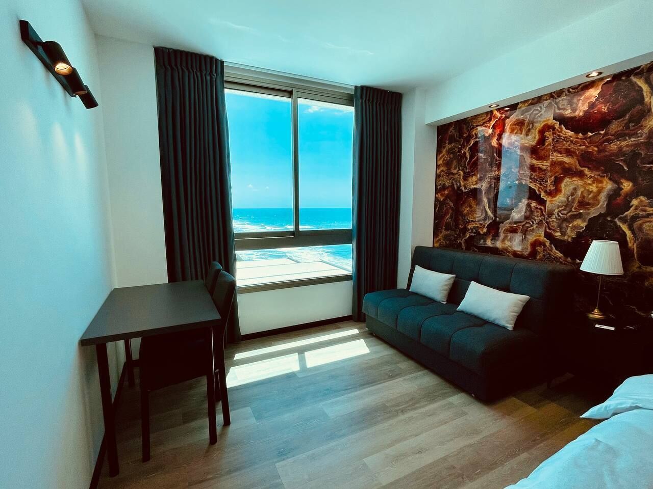 Et hotelværelse med stort vindue, sofa, bord og lampe.