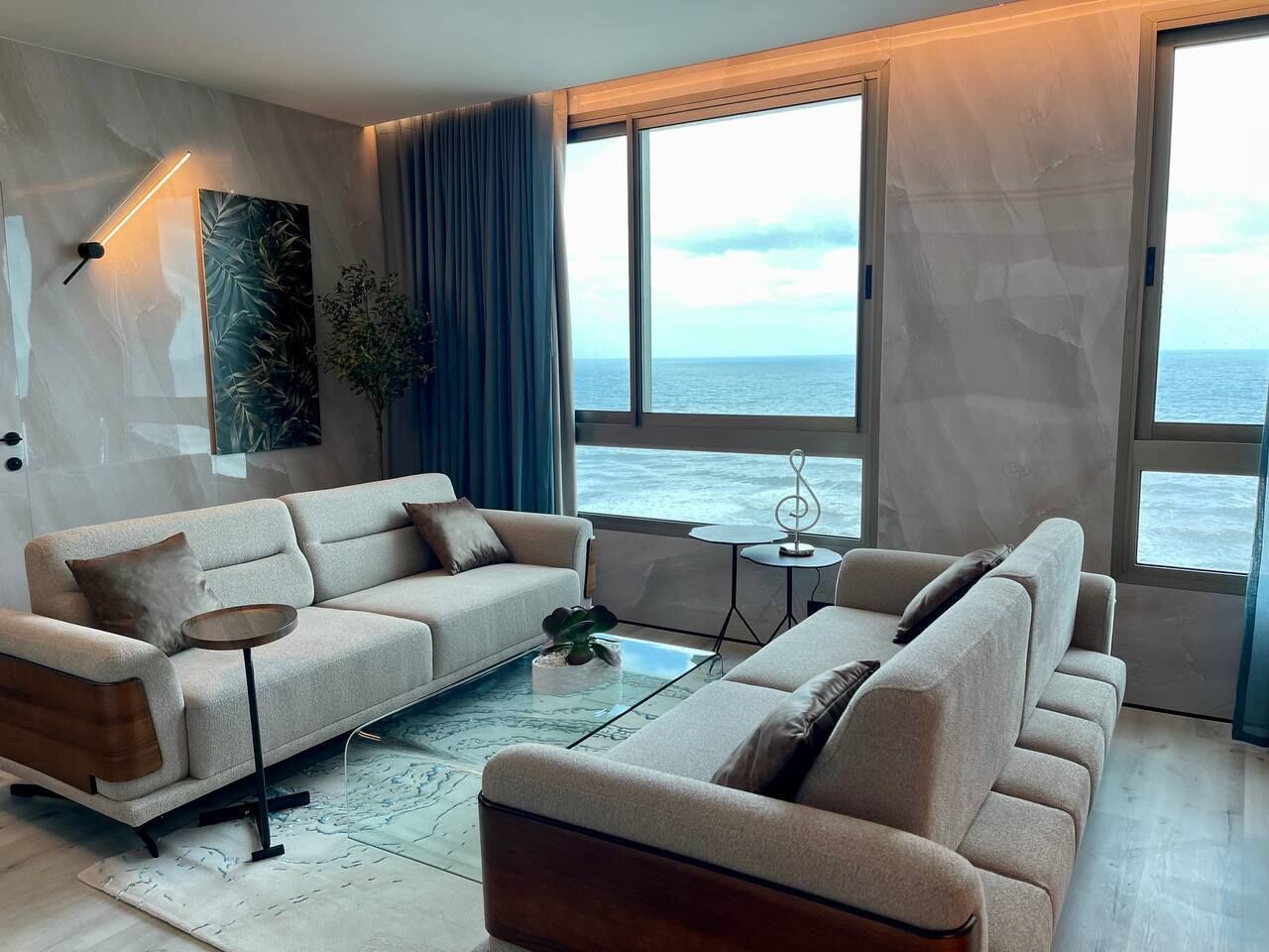 A modern living room with a sofa set, a coffee table, and a view of the sea.
