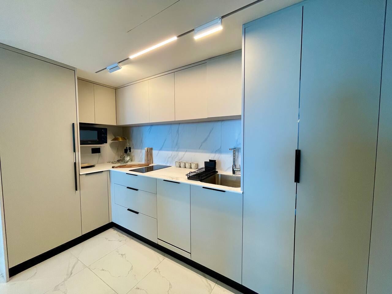 Una cucina moderna con mobili bianchi, un piano di lavoro nero e uno schienale in marmo.