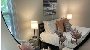A bedroom with a bed, two bedside lamps, a painting on the wall, and a window. - Serenity on Pinehurst No 6! <3.5 miles to the Village of Pinehurst! Sleeps 10! (Pine Hurst)
