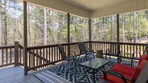 A covered outdoor deck with a glass table and chairs, surrounded by a wooden railing, overlooking a forested area. - Serenity on Pinehurst No 6! <3.5 miles to the Village of Pinehurst! Sleeps 10! (Pine Hurst)