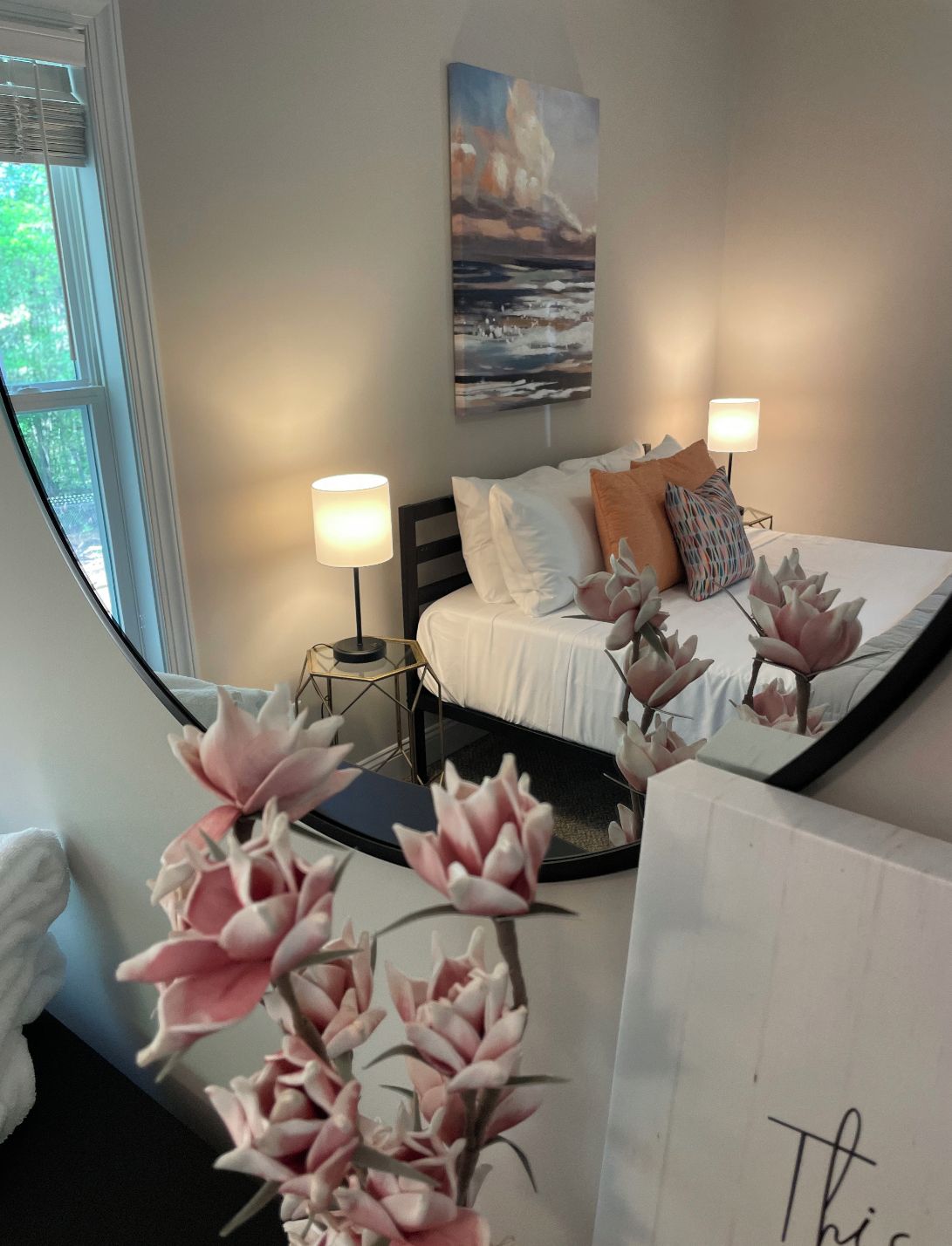 A bedroom with a bed, two bedside lamps, a painting on the wall, and a window.