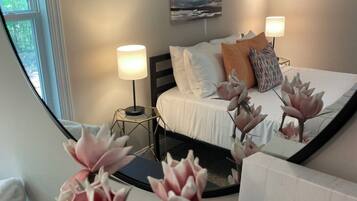 A bedroom with a bed, two bedside lamps, a painting on the wall, and a window.
