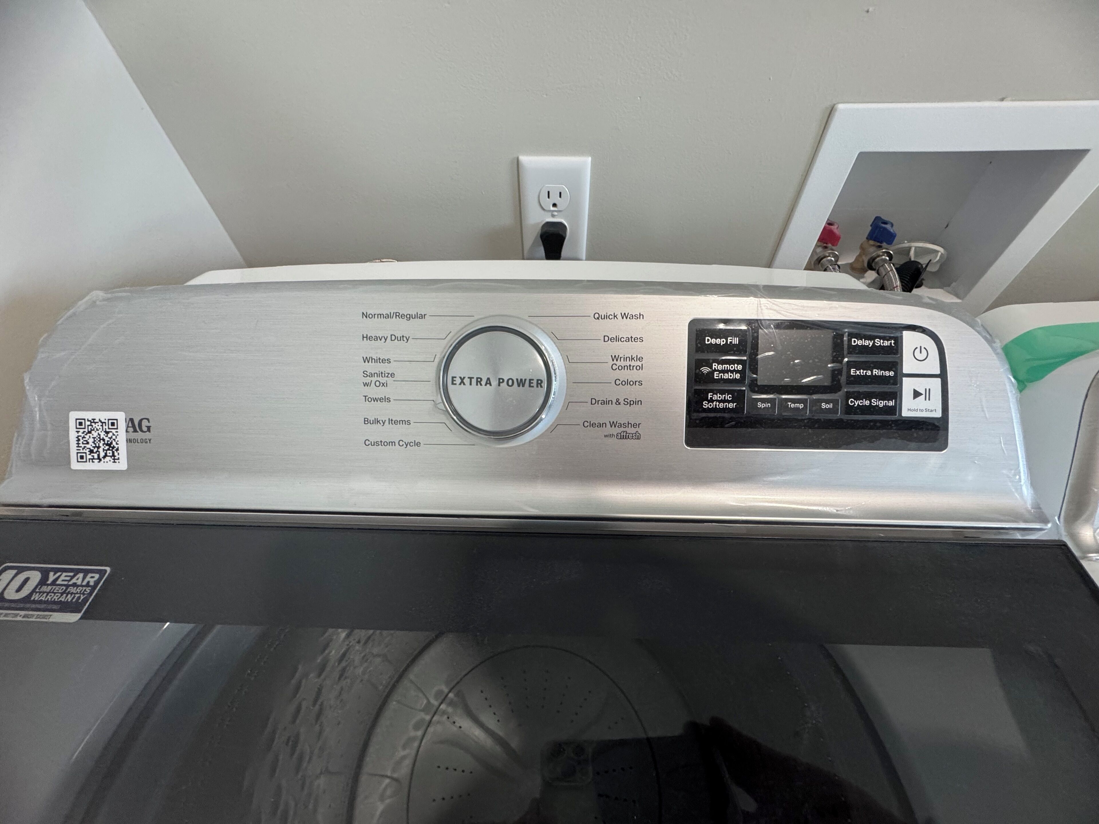 A front view of a washing machine with a control panel, a 10-year limited parts warranty sticker, and a QR code.