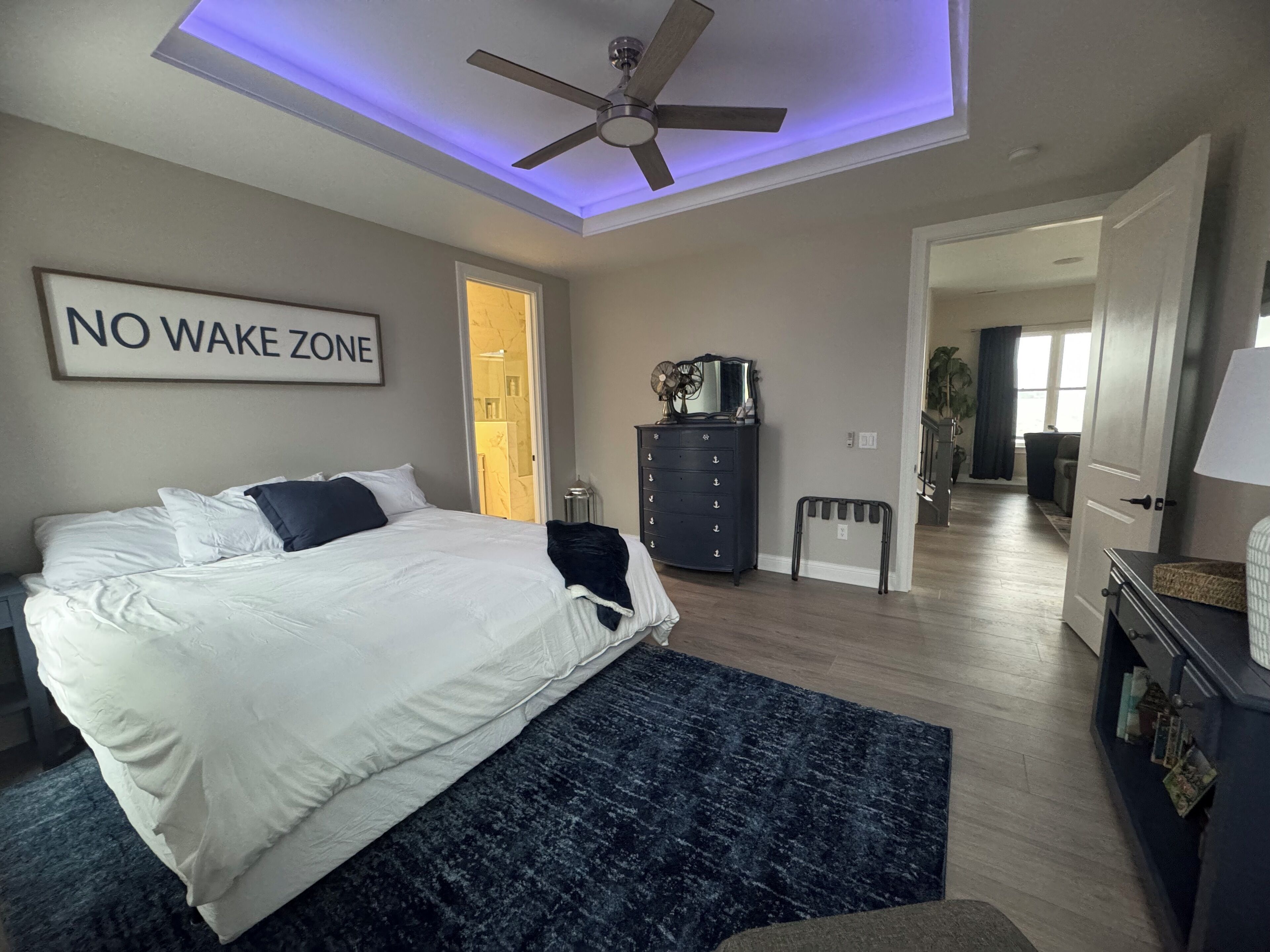 A bedroom with a bed, a ceiling fan, a dresser, and a 'NO WAKE ZONE' sign.
