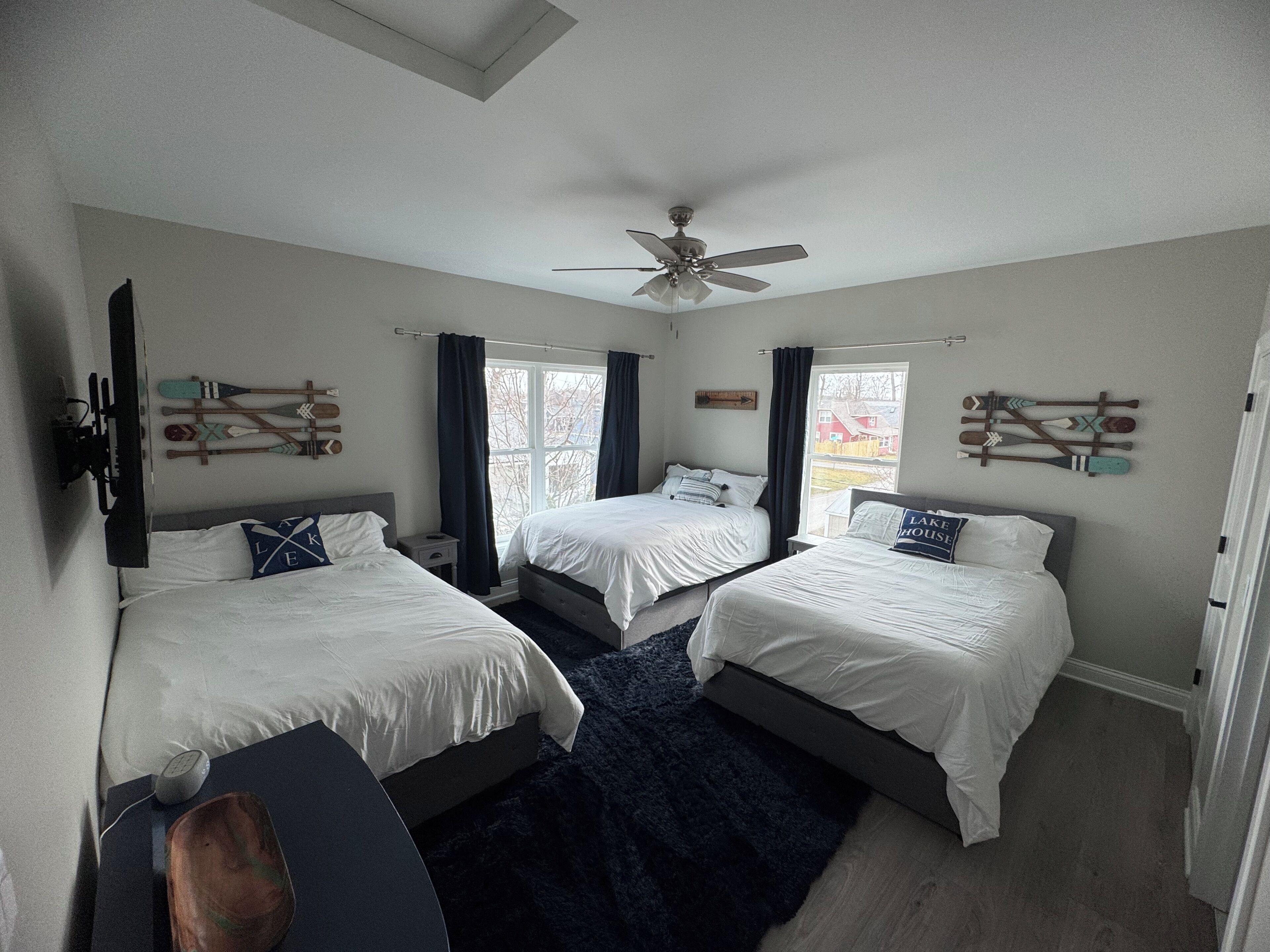 Une chambre avec deux lits, un ventilateur de plafond et des fenêtres avec des rideaux.