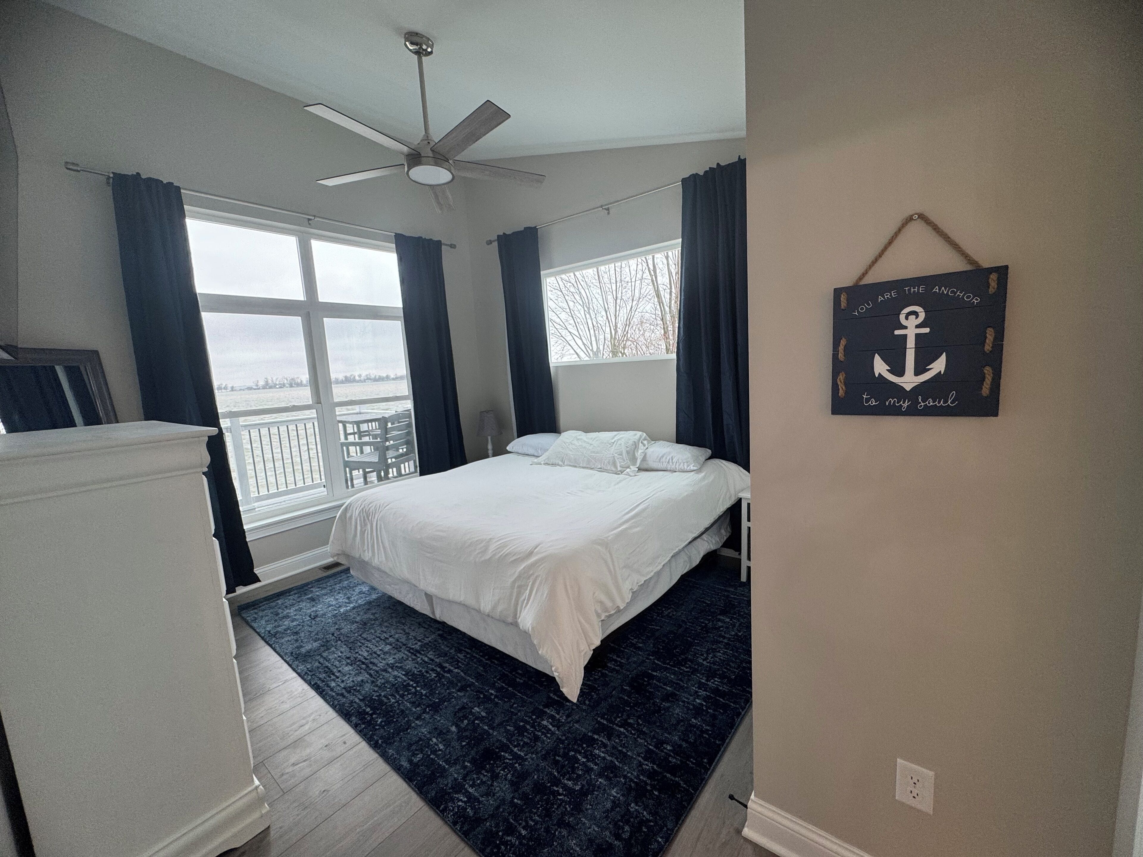 Une chambre avec un lit, un ventilateur de plafond, une vue sur la mer et une décoration murale inspirante.
