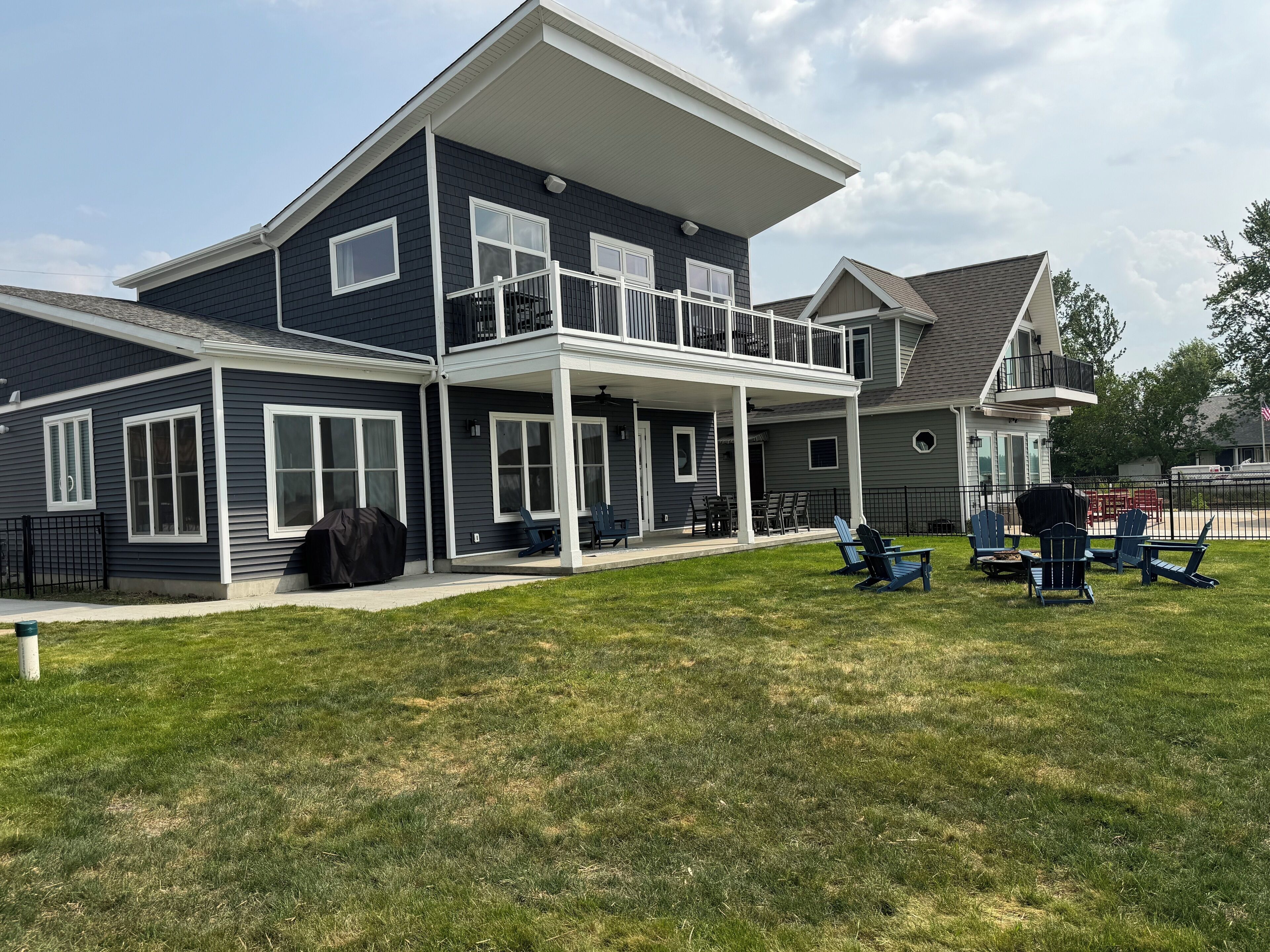 Ein zweistöckiges Haus mit überdachter Terrasse, Sitzgelegenheiten im Freien und Grillmöglichkeit.