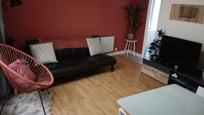 A living room with a black sofa, a pink chair, a white table, and a TV. - Pounette, T3 apartment center / Luxeuil thermal baths (Luxeuil-les-Bains)