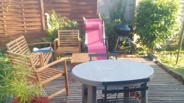 An outdoor patio area with a round table and wooden chairs, surrounded by a wooden deck and a brick wall. - Pounette, T3 apartment center / Luxeuil thermal baths (Luxeuil-les-Bains)