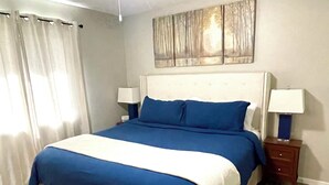 Une chambre à coucher avec un grand lit, deux tables de chevet avec des lampes, une tête de lit et un tableau au mur.