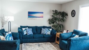 Un salon avec un canapé turquoise, un tapis à motifs et une grande plante.