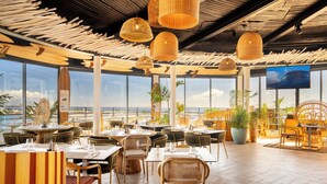 Een restaurant met tropisch thema, met rieten meubels, grote ramen en uitzicht op de oceaan.