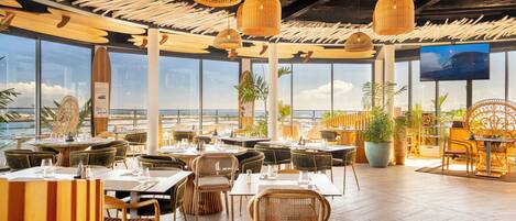 A restaurant with a tropical theme, featuring wicker furniture, large windows, and a view of the ocean.