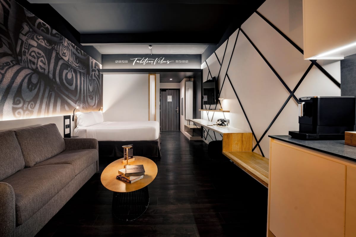 Een moderne hotelkamer met een bank, een ronde salontafel met boeken, een bed, een bureau met een lamp en een televisie.