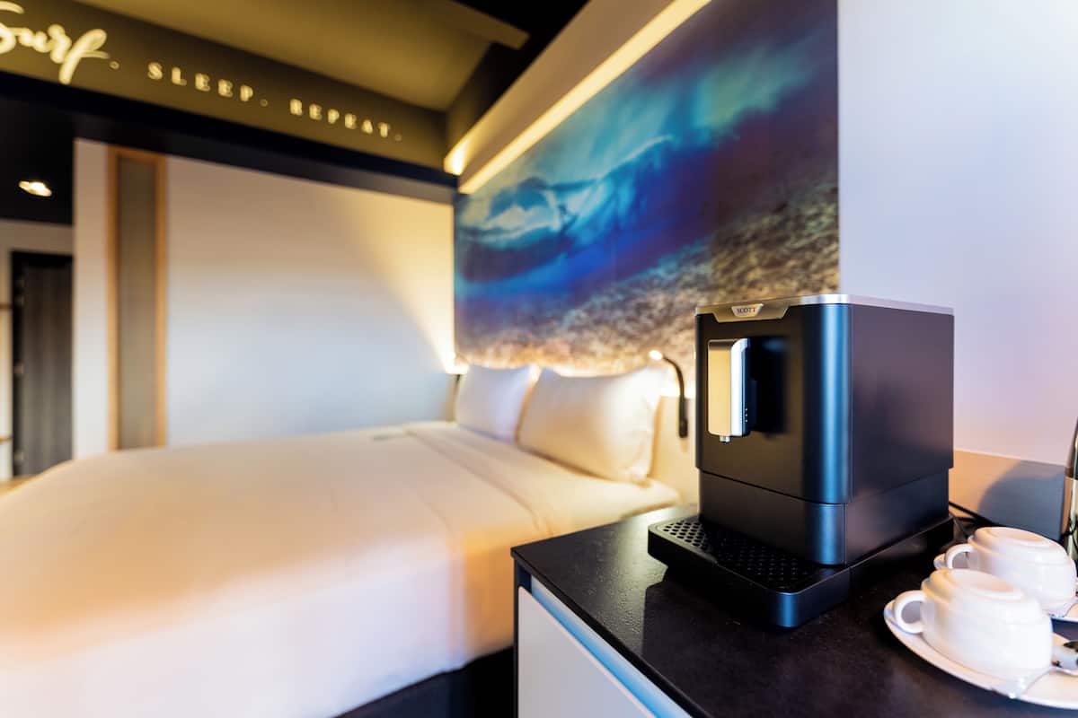 Een moderne hotelkamer met een bed, een koffiezetapparaat en twee kopjes op een tafel.