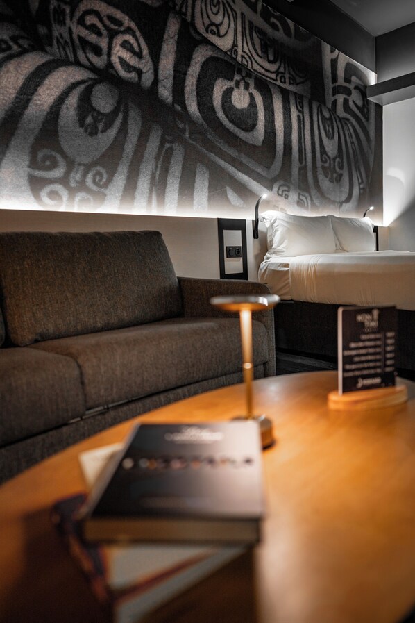 A hotel room with a bed, a sofa, a table with a lamp, and a wall with a decorative pattern. - Boutique Hotel Kon Tiki Tahiti (Papeete)