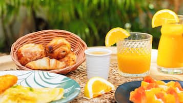 A breakfast setting with croissants, orange juice, and fruit on a wooden table outdoors.
