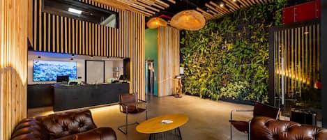 A modern interior with a reception desk, leather sofas, a round table, and a green wall with plants.