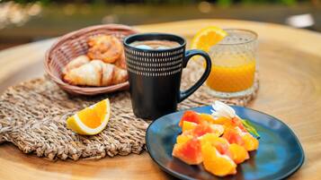 A breakfast setting with croissants, a black mug, a plate of fruit, and a glass of orange juice on a woven placemat.