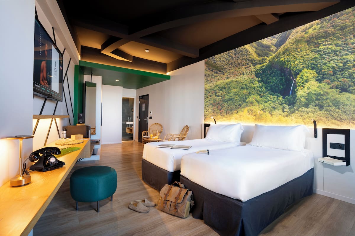 Een moderne hotelkamer met een groot bed, een bureau met telefoon en uitzicht op een bebost landschap.