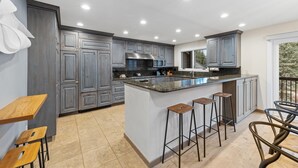 A modern kitchen with grey cabinets, a central island with stools, and a large window providing a view of the outdoors.
