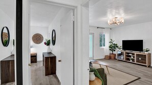Ein modernes Wohnzimmer mit Holzboden, einem Fernseher, einer Chandelier und einem Essbereich mit Tisch und Stühlen.