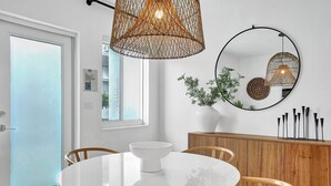 Ein Essbereich mit einem runden weißen Tisch, Holzstühlen, einer weißen Vase mit Grünpflanzen, einem Holzschrank und zwei Pendelleuchten.