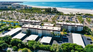 A multi-story hotel with a parking lot, surrounded by palm trees and a beach. - Condo# 107  Two minutes walk to the Beach! (Sarasota)