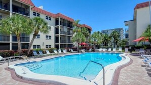 A pool area with lounge chairs and palm trees, surrounded by multi-story buildings with balconies. - Condo# 107  Two minutes walk to the Beach! (Sarasota)