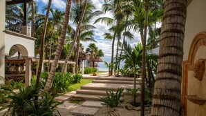 A tropical resort with a palm tree-lined pathway leading to a thatched-roof structure. - BEACHFRONT LUXURY VILLA ON A PRIVATE BAY (Tulum)
