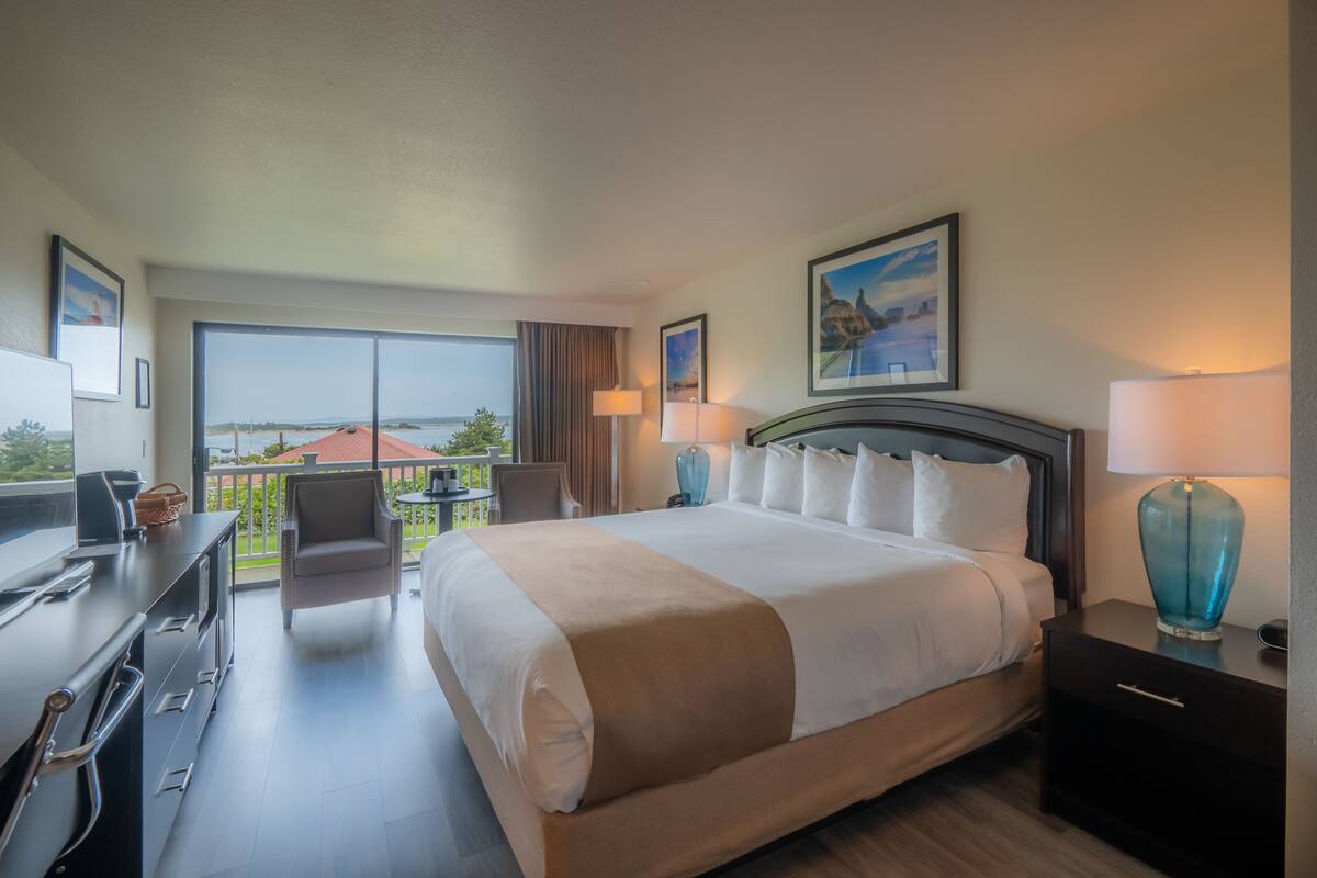 A hotel room with a large bed, a desk, a chair, and a balcony with a view.