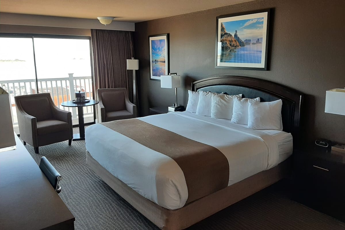 A hotel room with a large bed, two armchairs, a small table, and a balcony.