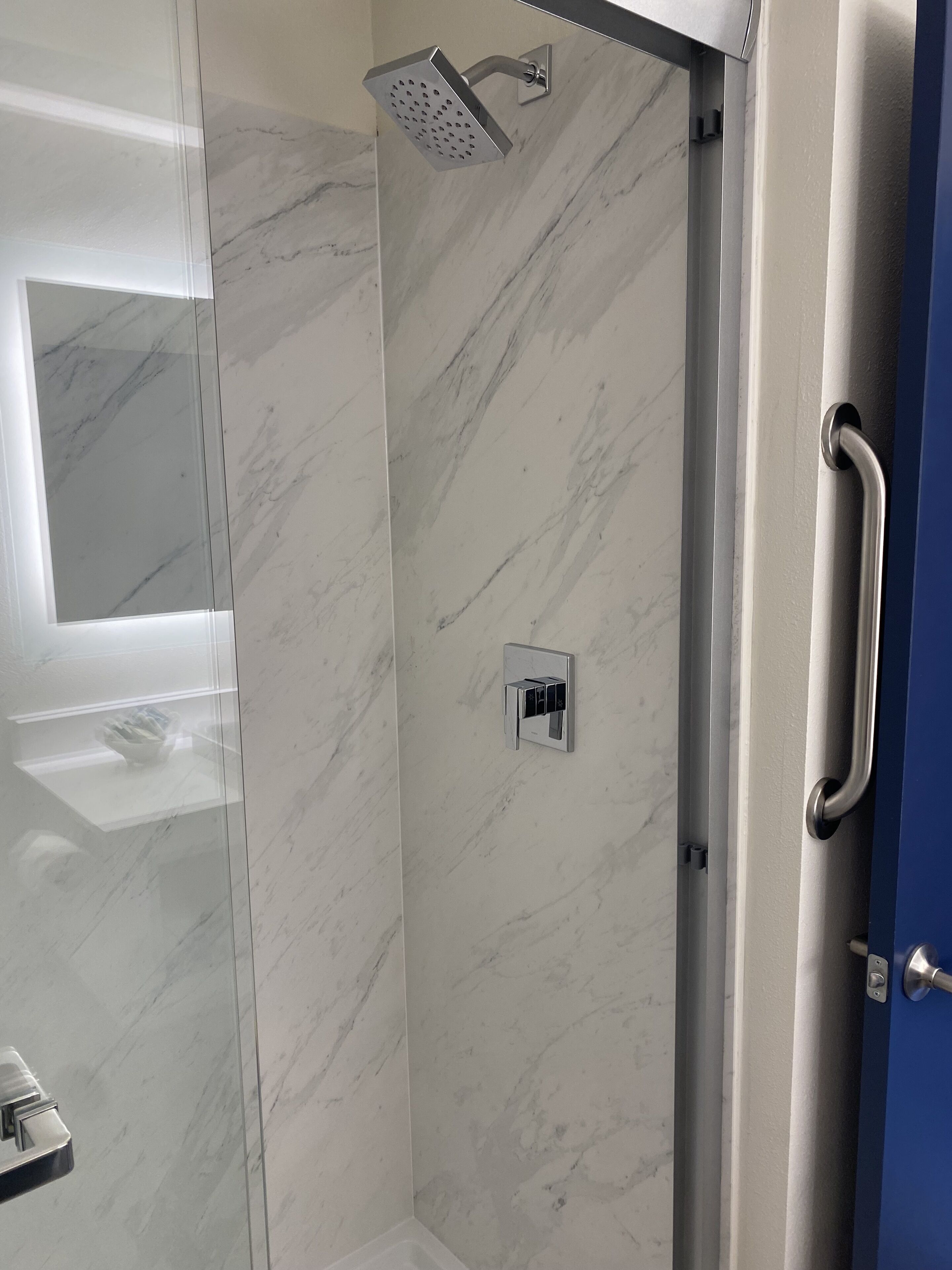 A modern bathroom with a glass shower enclosure, a marble wall, and a built-in towel rack.