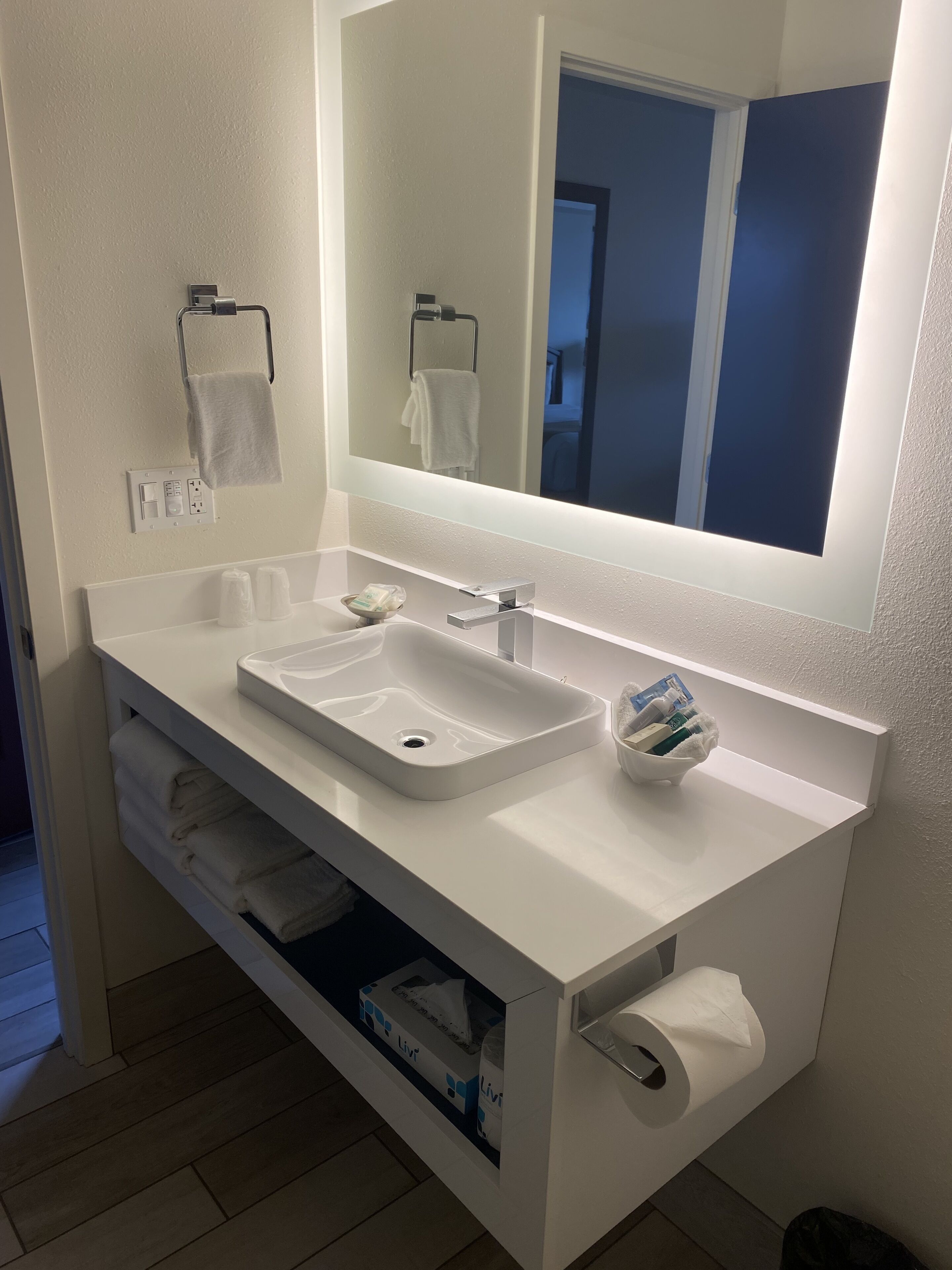 Un baño moderno con un lavamanos blanco, un espejo, un perchero para toallas y un dispensador de papel higiénico.