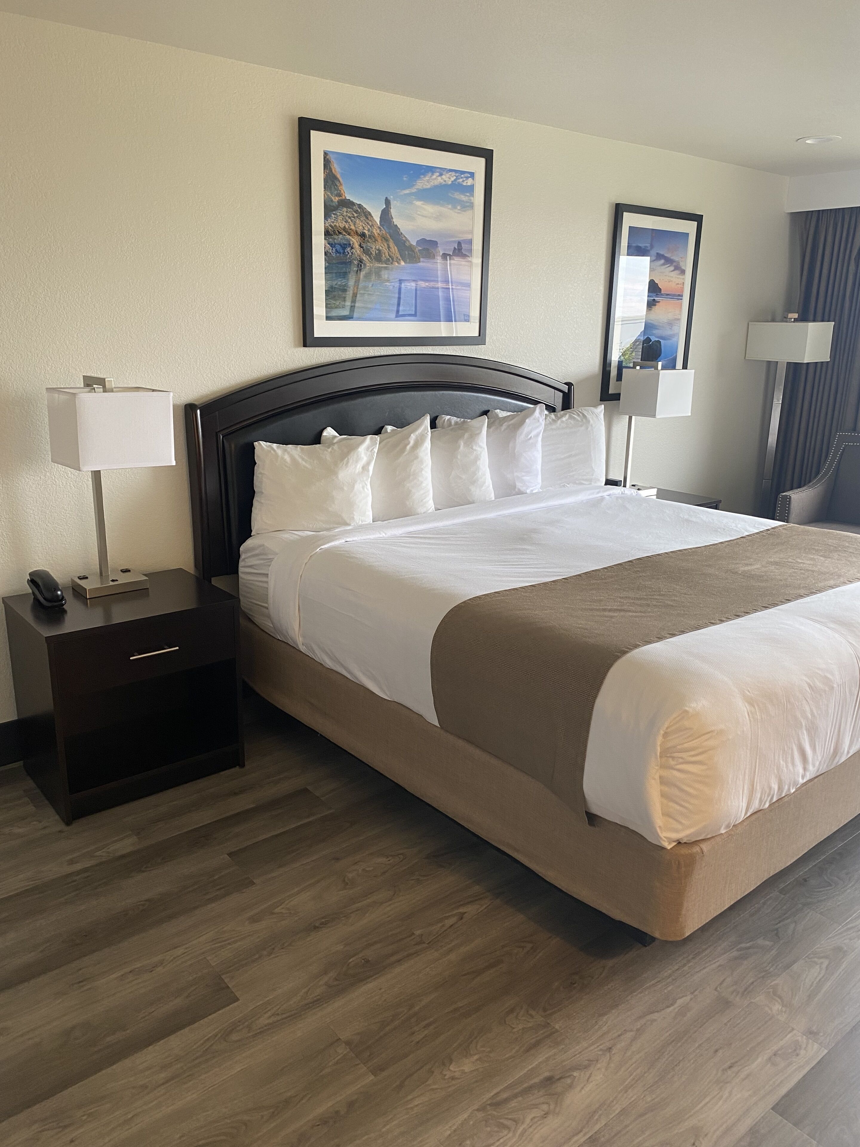 Een hotelkamer met een groot bed, een nachtkastje, een bureau en twee ingelijste foto’s aan de muur.
