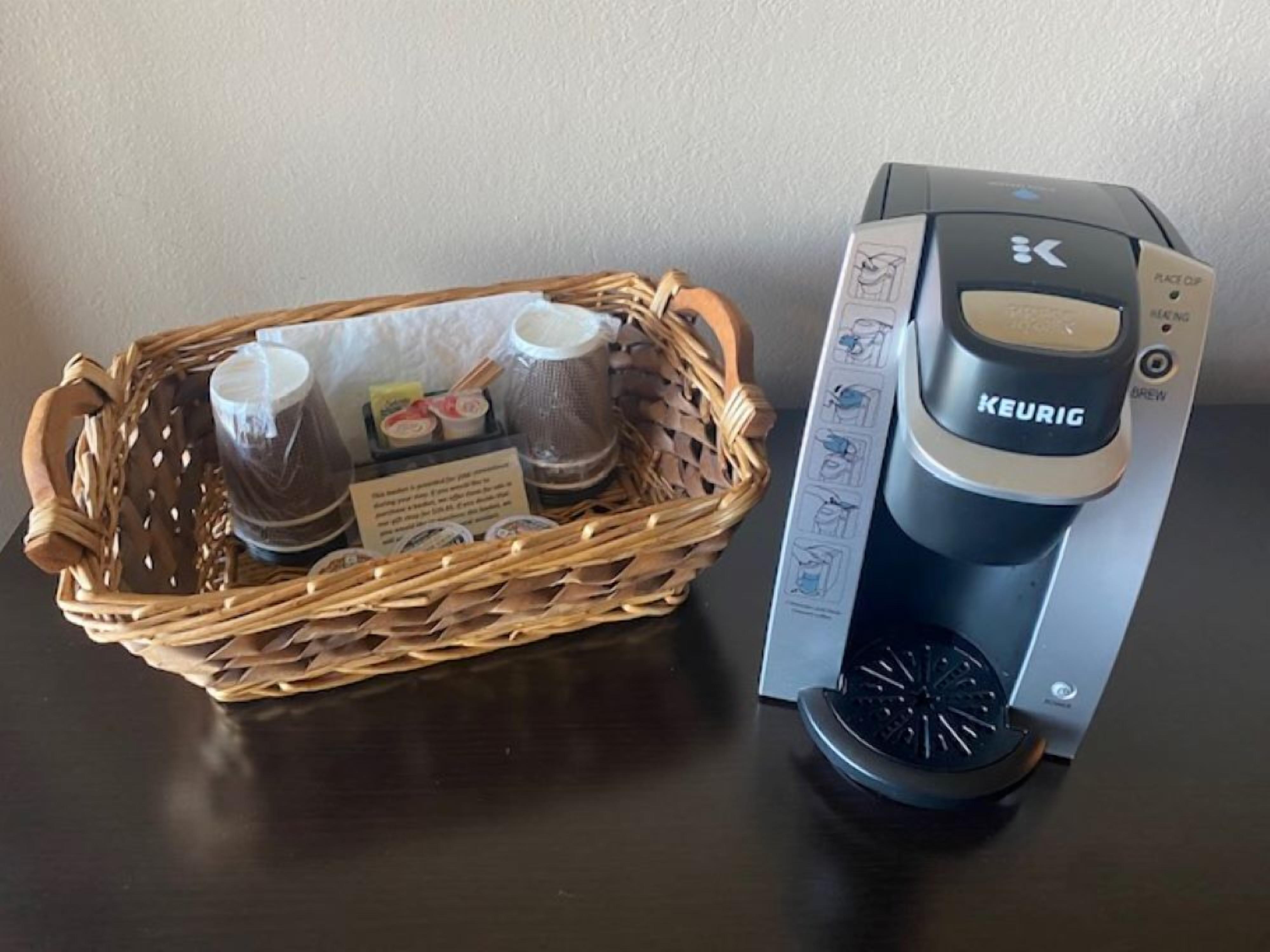 A Keurig coffee maker next to a wicker basket containing coffee pods and a reusable cup.
