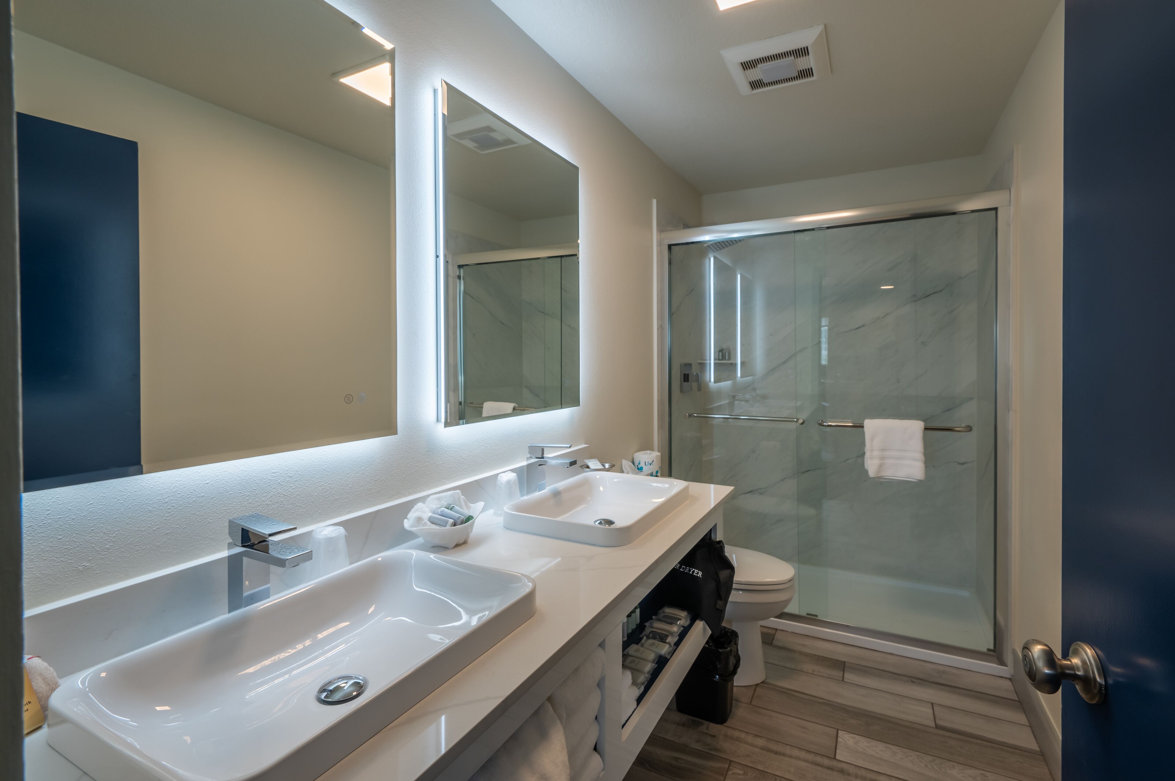 Une salle de bain moderne avec un grand miroir, deux lavabos, une douche et des toilettes.