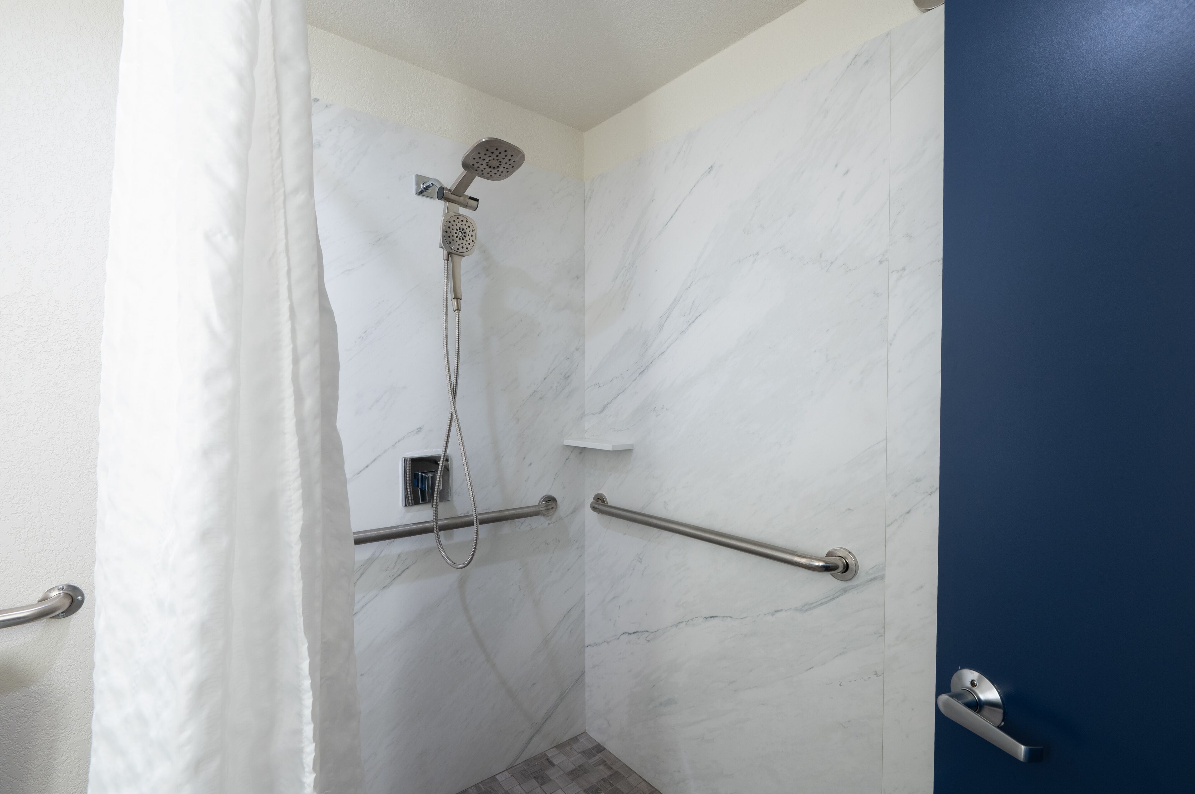 A bathroom with a shower, marble walls, and a blue door.