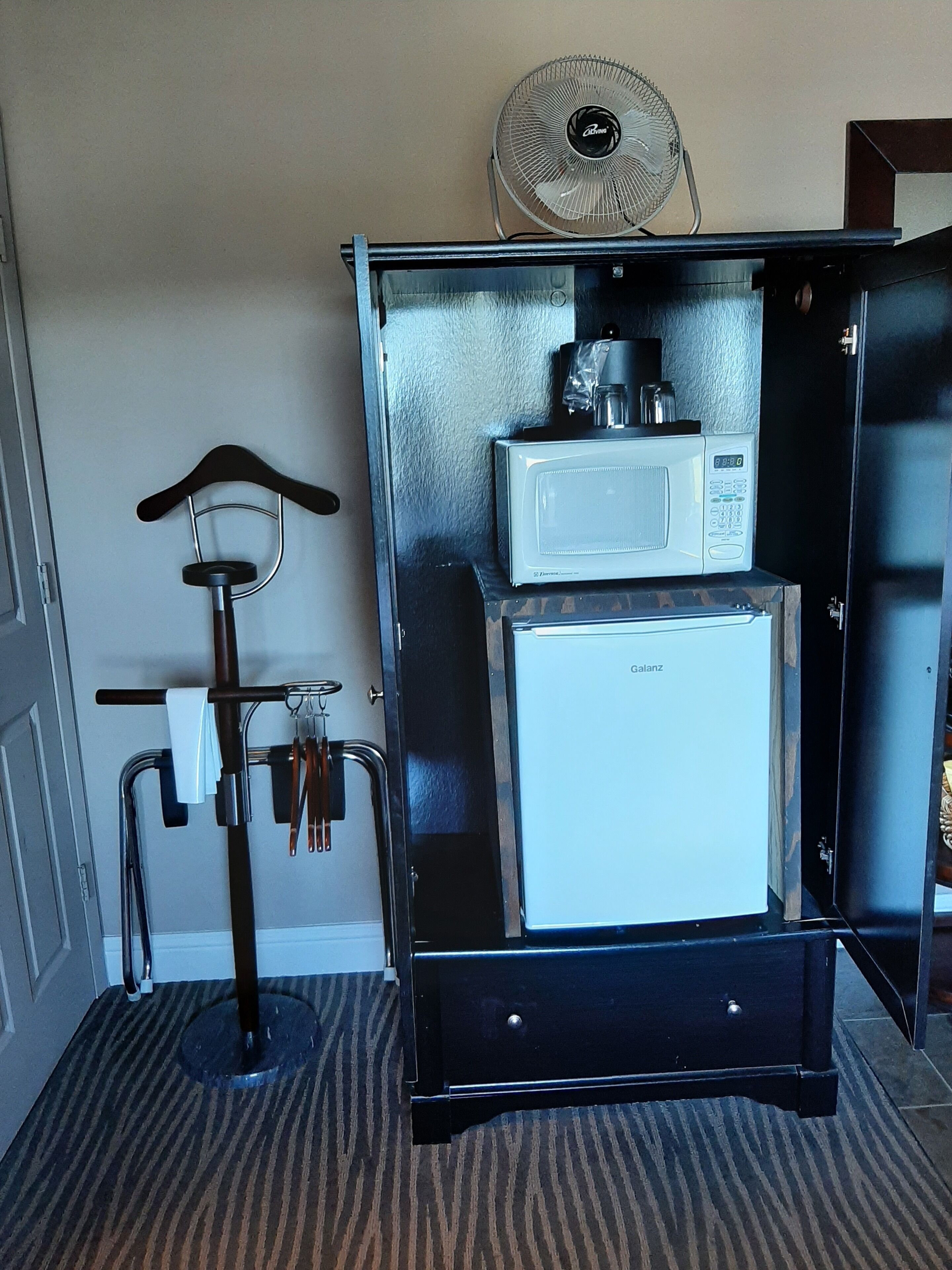 A compact kitchenette with a microwave and refrigerator, a small fan, and a bicycle rack.