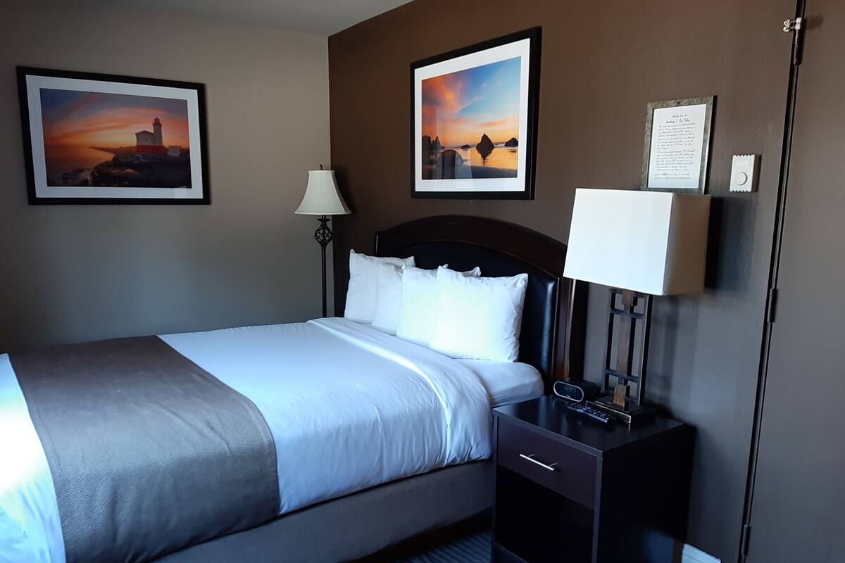 A hotel room with a bed, bedside table, lamp, and two framed pictures on the wall.