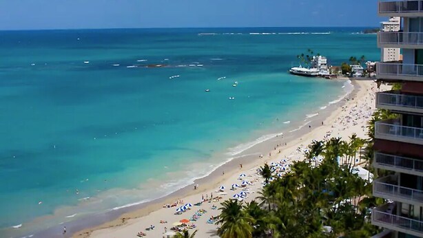 A beach with clear turquoise waters, a sandy shore, and a building with balconies overlooking the beach. - Luxurious Ocean View Studio Next to Major Hotels (Carolina)
